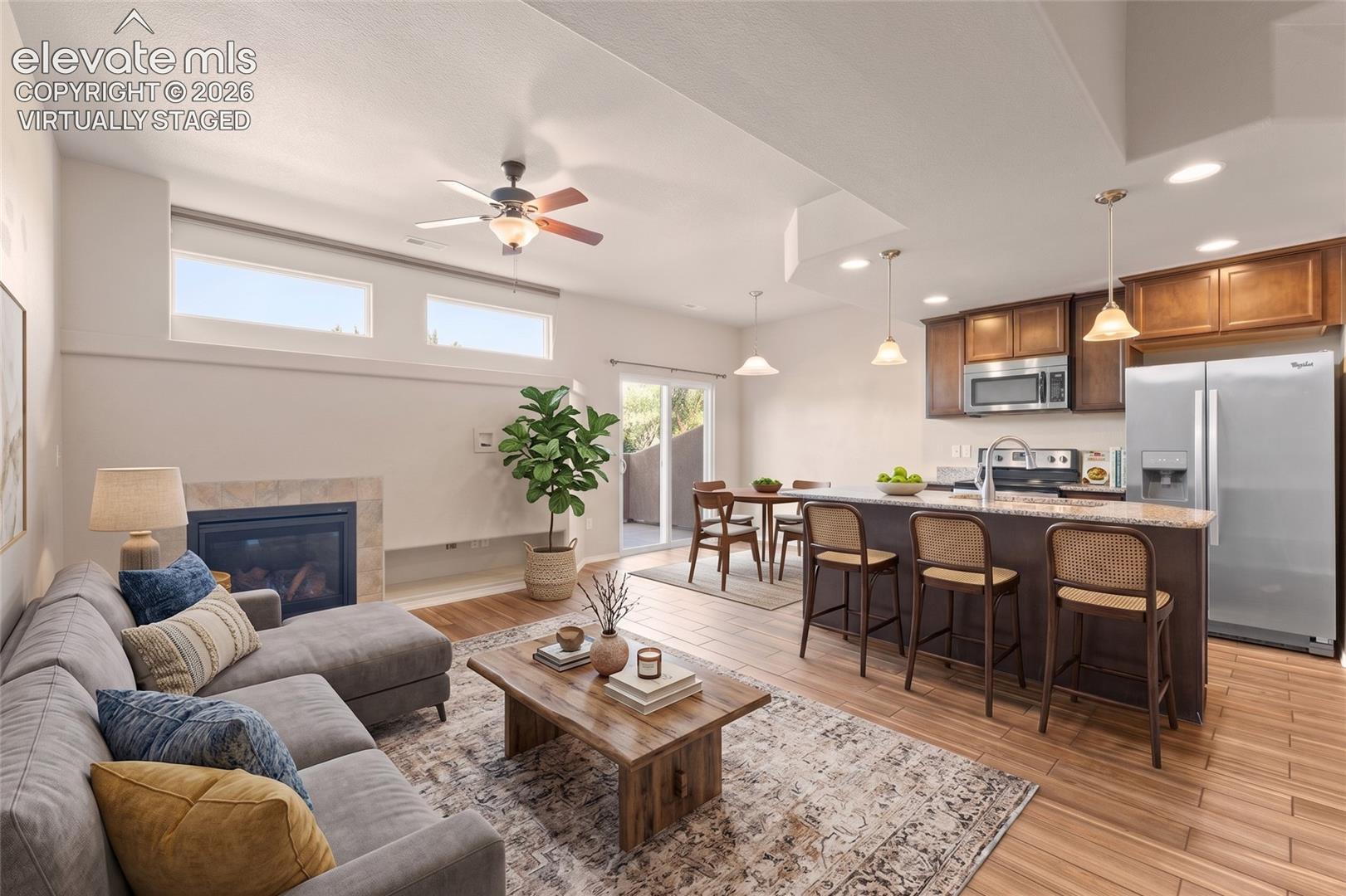 Open-concept living area featuring a fireplace with stone surround, wood-finish flooring, and a ceiling fan - virtually staged