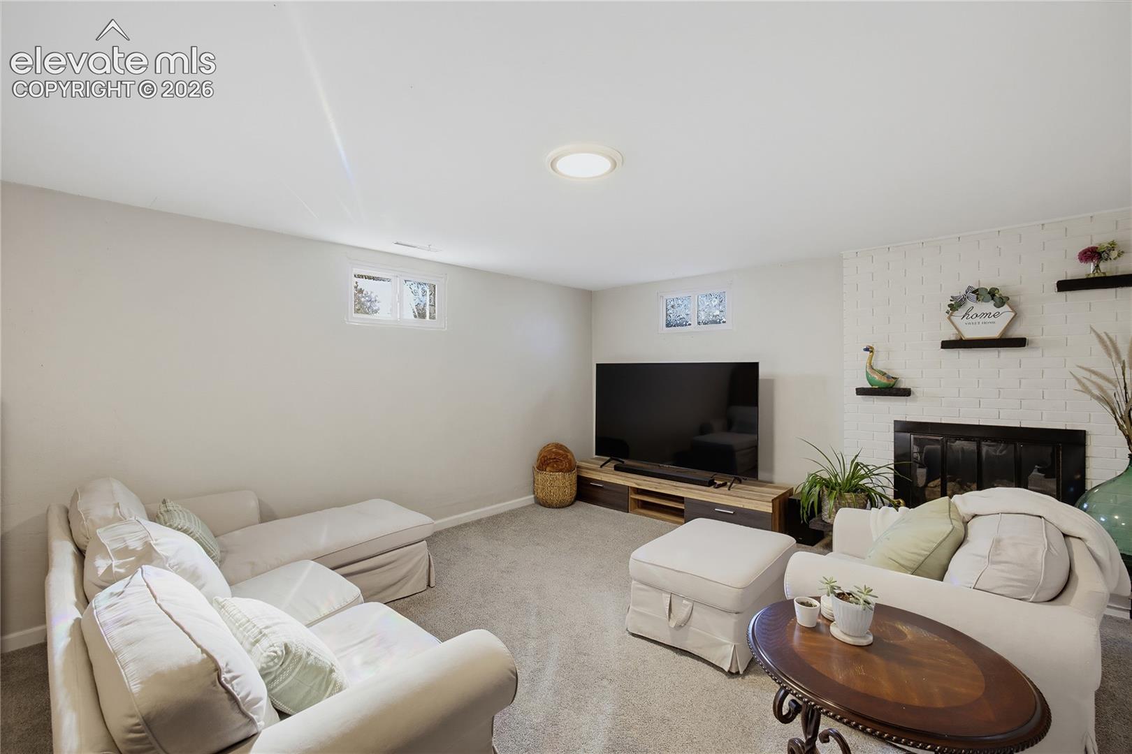 Recessed ceiling lighting, carpeted flooring, two permanent windows, painted brick fireplace surround, and built-in fireplace insert