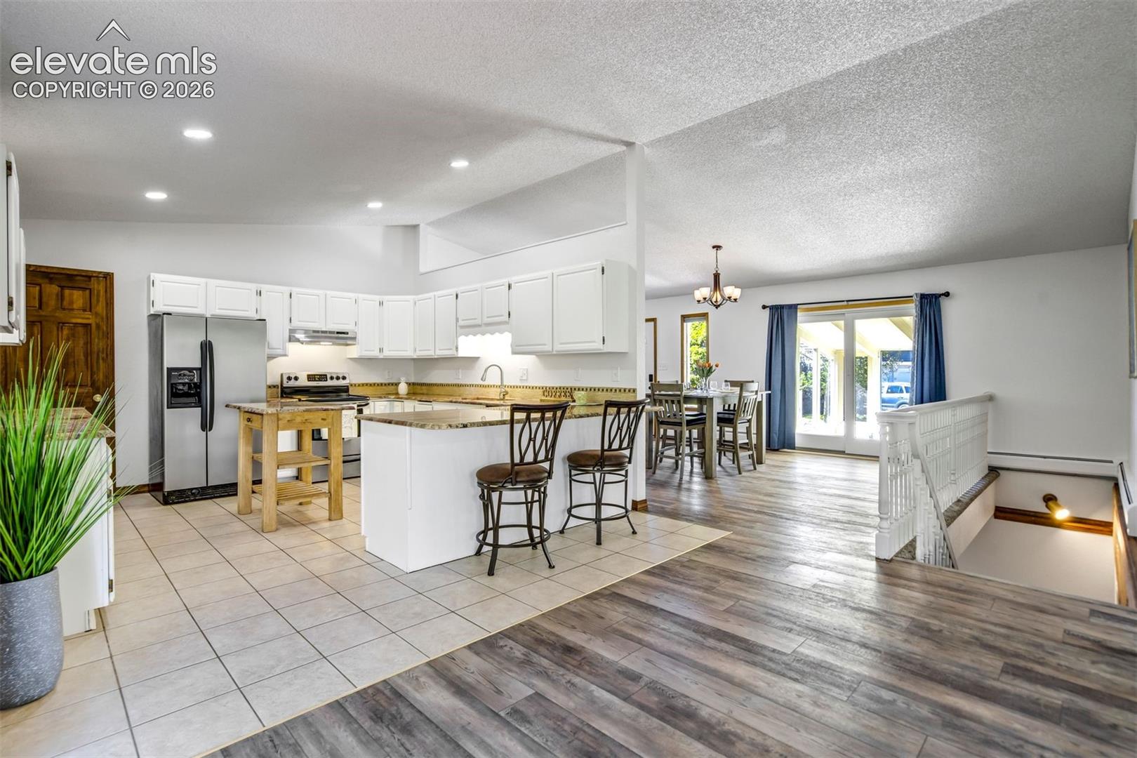 Spacious open-concept kitchen featuring white cabinetry, stainless steel appliances, and granite-look countertops