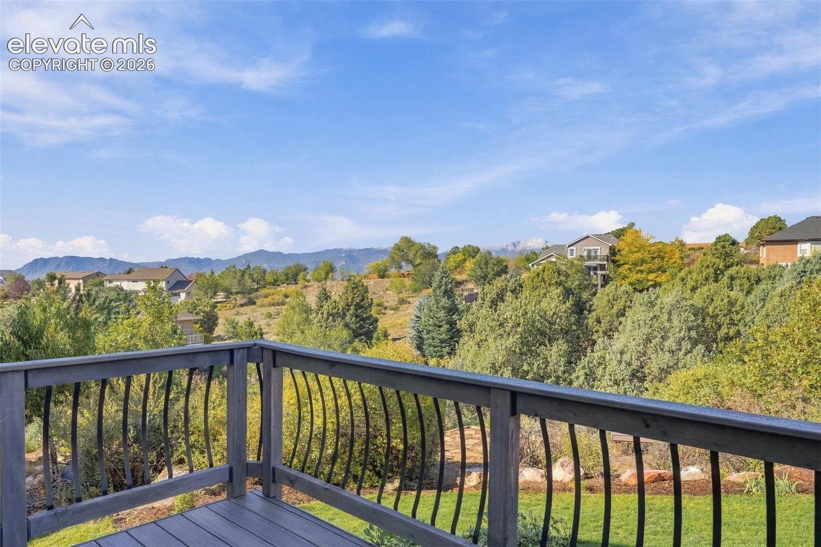 Elevated deck with dark-finish wood composite decking and black metal balustrade featuring a curved design, overlooking an expansive natural landscape with mountain backdrop