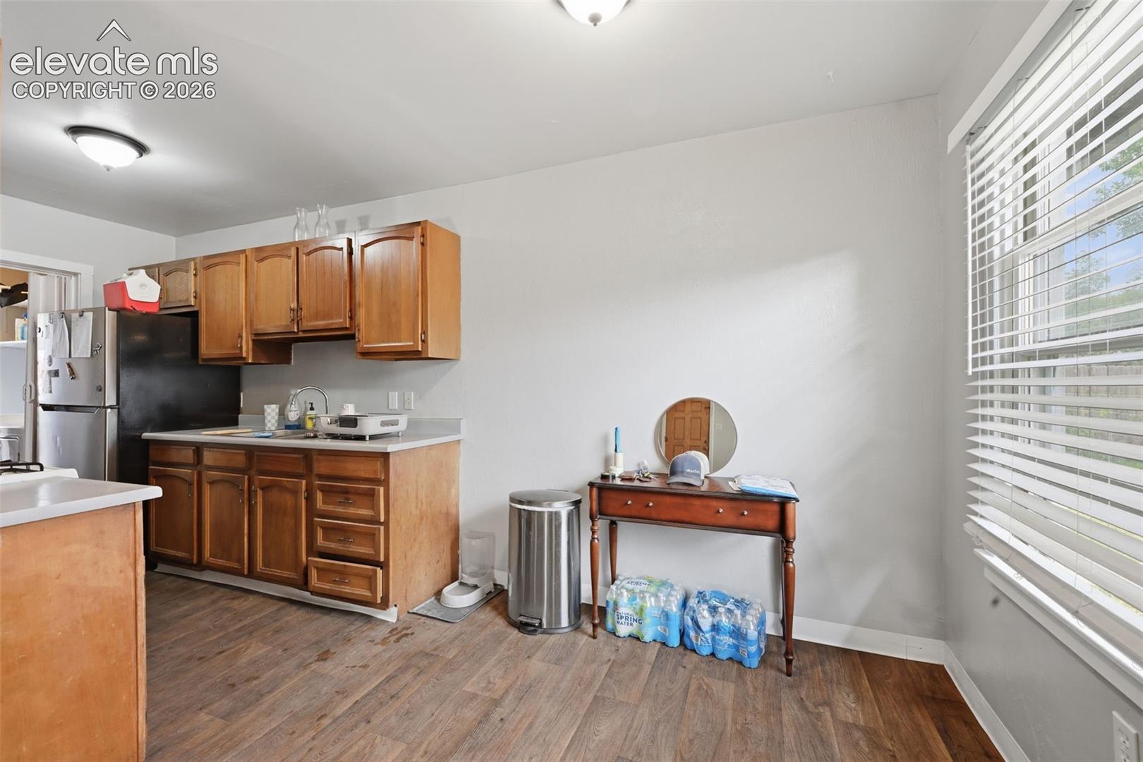 Kitchen and dining area featuring wood-finish flooring, wood cabinetry, light countertops, and a window with blinds