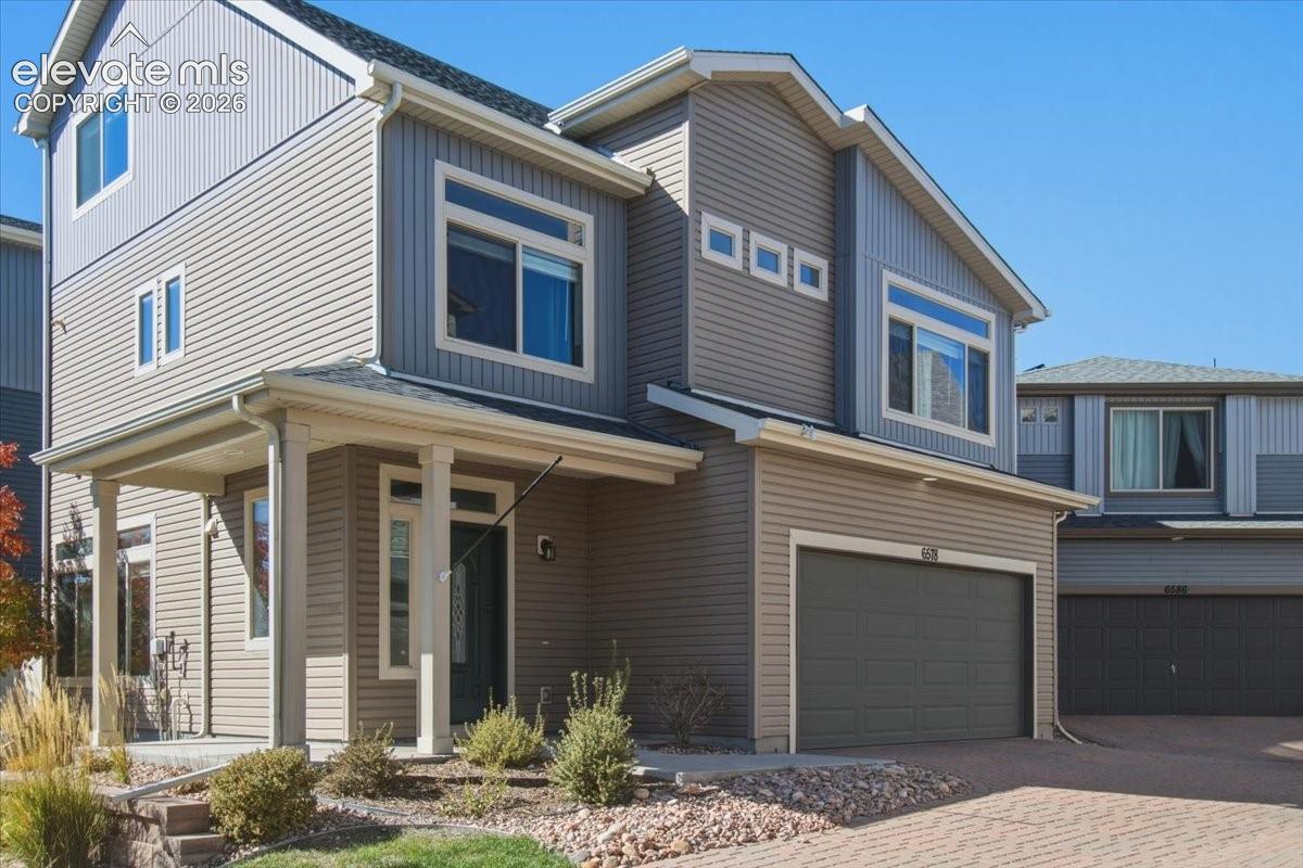 Two-story residence featuring a covered front porch, an attached garage, and a paver driveway