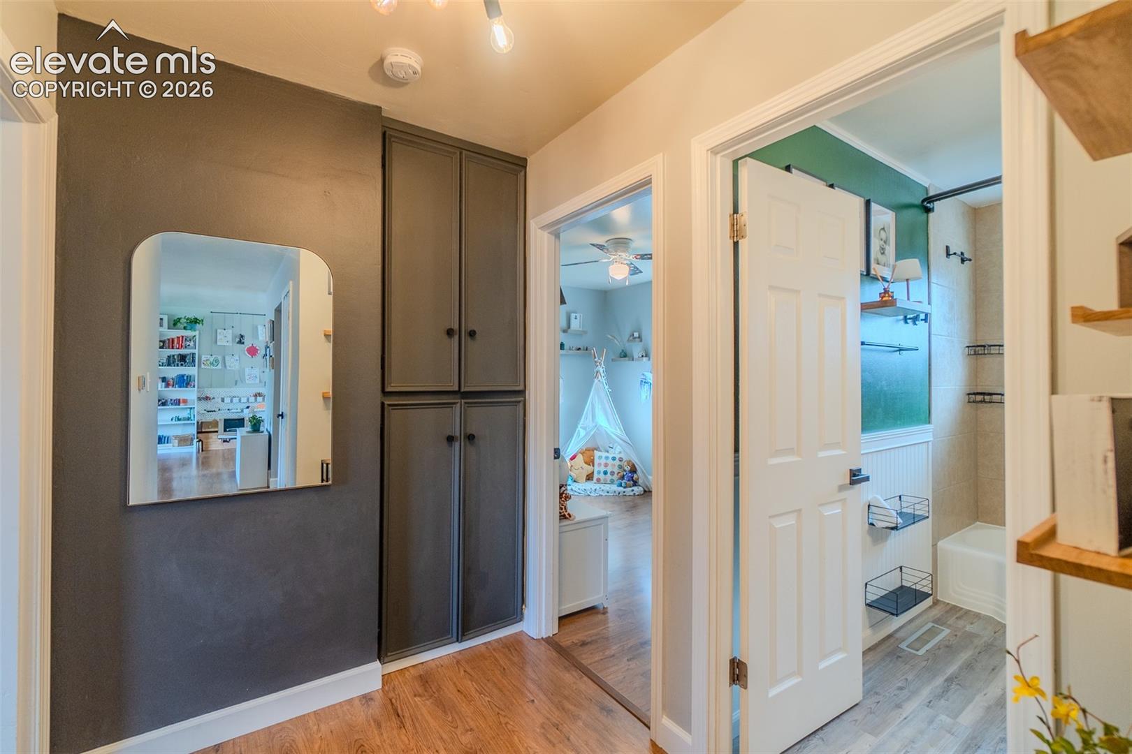 Hallway featuring tall built-in cabinetry, wood-finish flooring, and a wall-mounted arched mirror