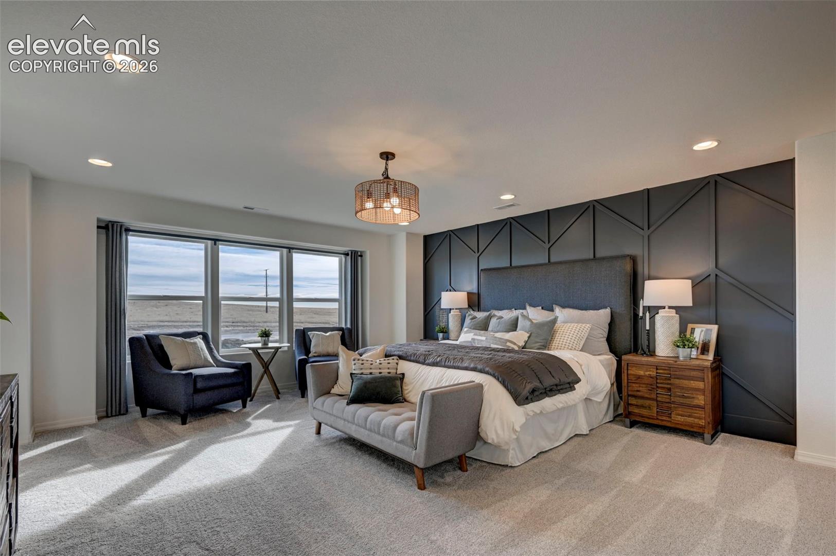 primary bedroom with dark geometric accent wall, upholstered headboard, and large three-panel window with seating