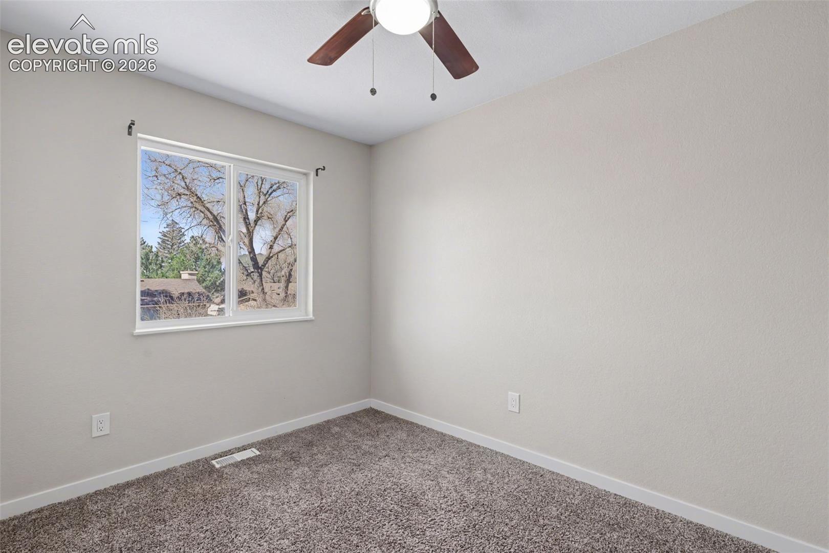 Room featuring neutral wall tones, wall-to-wall carpeting, a large sliding window, and a ceiling-mounted light fixture with a fan