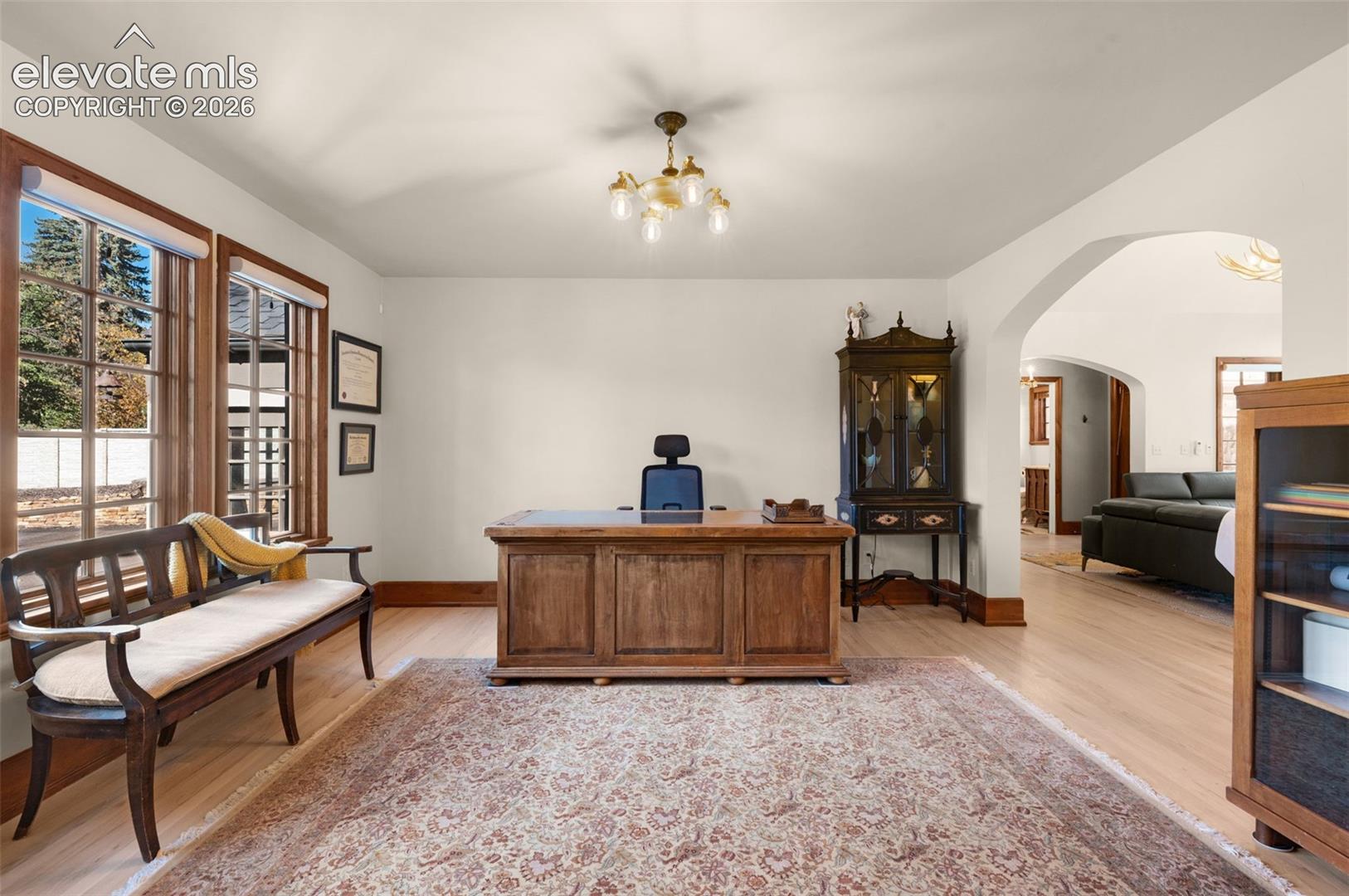 Light-filled room featuring wood-finish flooring, multi-pane windows with wood trim, an arched architectural opening, and a classic multi-arm chandelier
