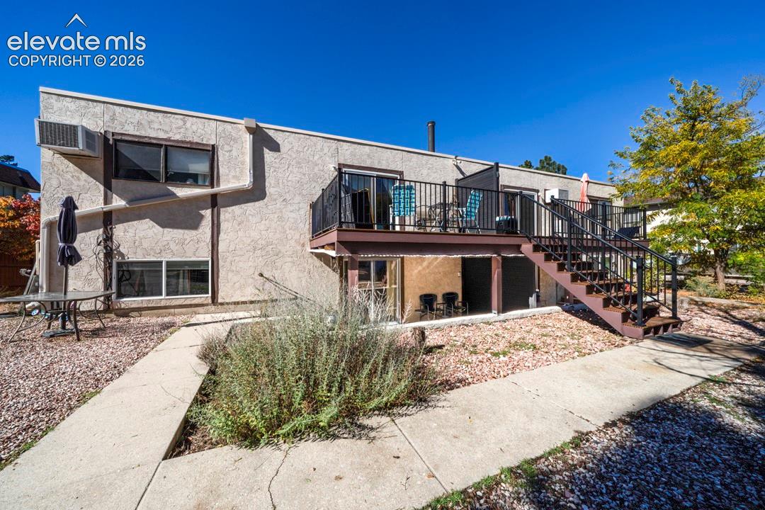 Stucco exterior featuring a raised wooden deck with metal railing, an external staircase, and a concrete patio