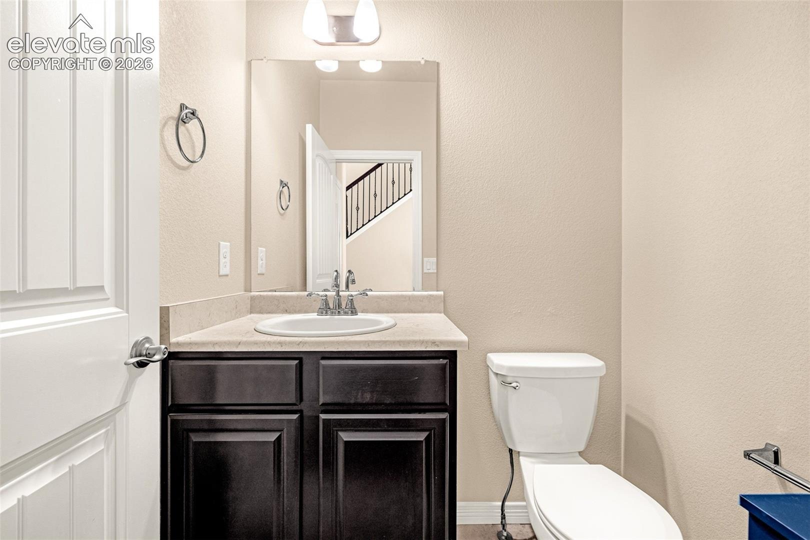 Recessed sink with a chrome faucet, dark wood-finish cabinetry, light-toned countertop, and a white toilet