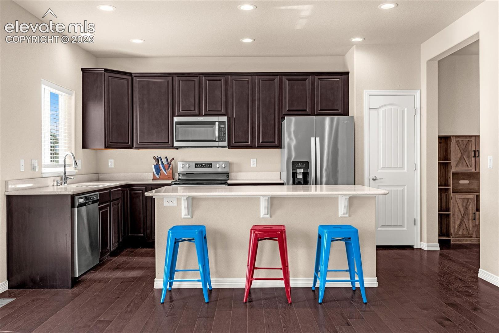 Kitchen featuring dark wood-finish cabinetry, light countertops, stainless steel appliances, a kitchen island with seating, and recessed lighting