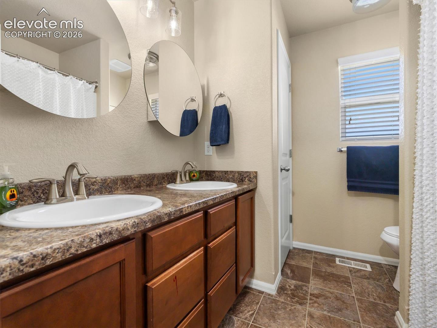 Dual vanity with integrated sinks, wood-finish cabinetry, and a patterned countertop