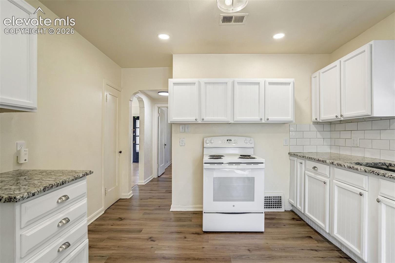 Kitchen featuring white shaker-style cabinetry, stone-finish countertops, subway tile backsplash, recessed lighting, and wood-finish flooring
