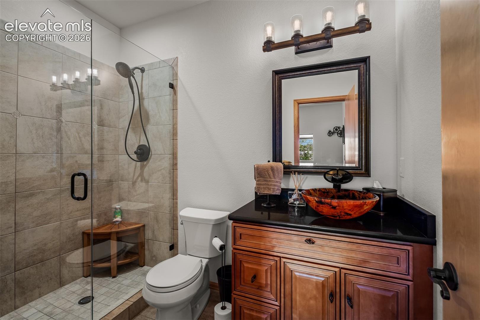 Walk-in shower with clear glass enclosure custom tile and bowl sink serving the lower level.