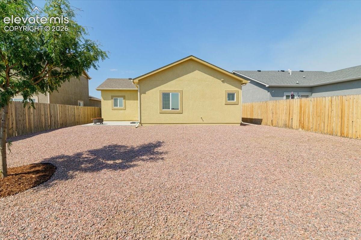 Expansive gravel yard with wood privacy fencing, a mature tree, and a stucco exterior