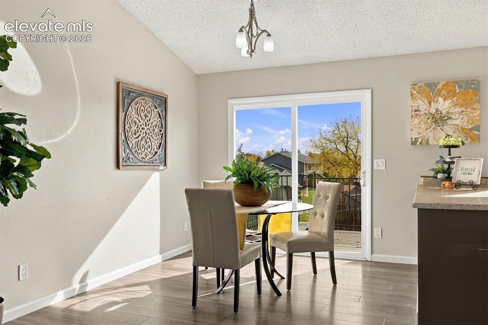 Wood-finish flooring, vaulted ceiling, three-light chandelier fixture, and sliding glass door with access to an exterior deck