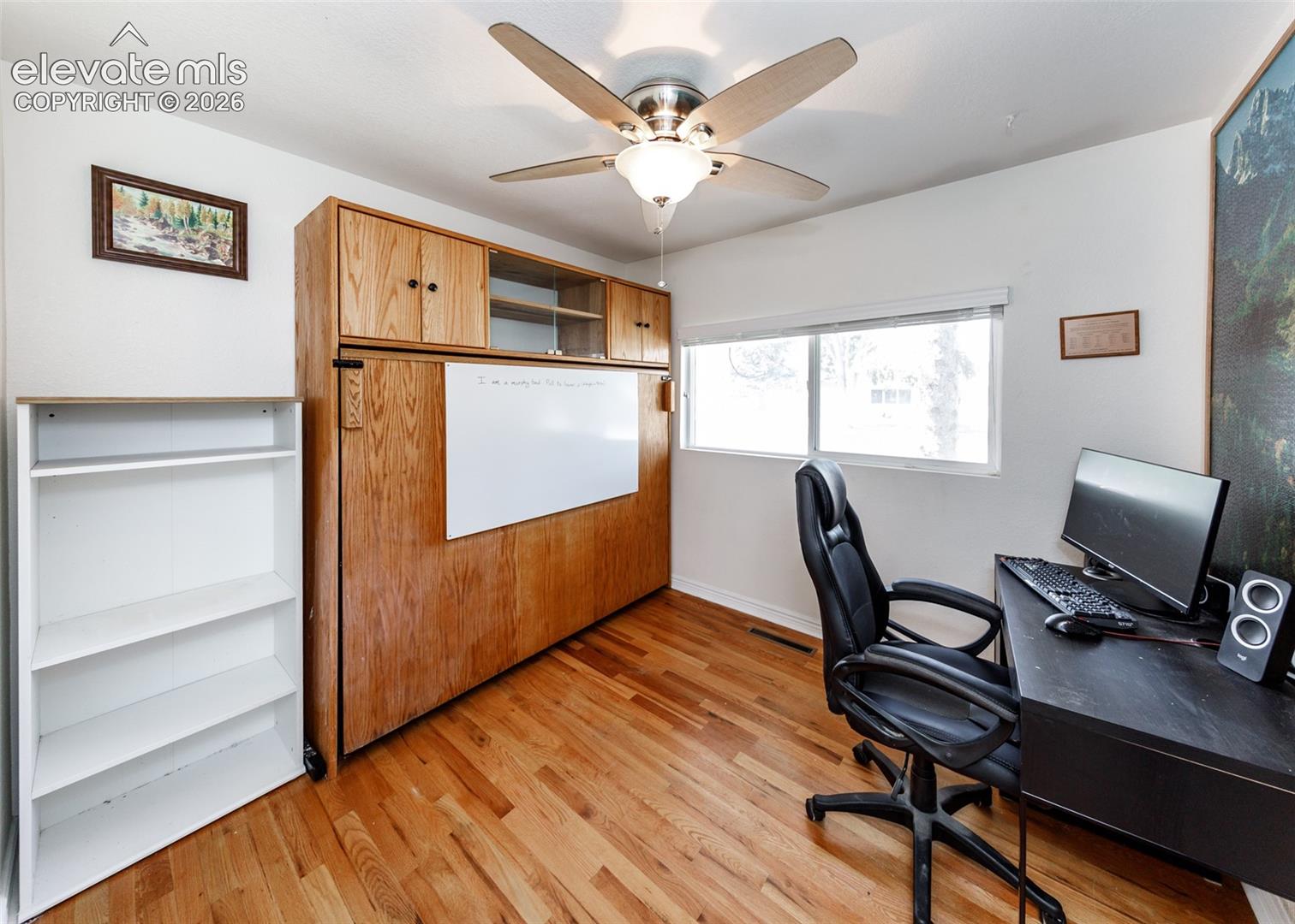 Wood-finish flooring, built-in cabinetry with integrated whiteboard, and a ceiling fan with integrated lighting
