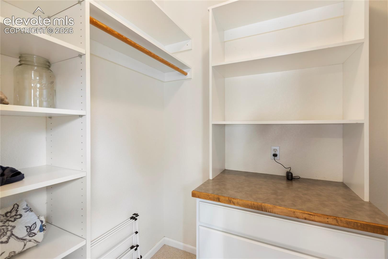 Custom closet system featuring white shelving units, a natural wood-finish hanging rod, white drawers, and a wood-finish countertop
