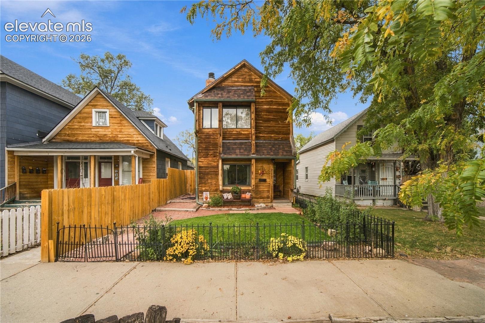 Two-story wood-clad residence featuring a front gabled roofline, metal perimeter fencing, manicured lawn, and stone-paved walkway
