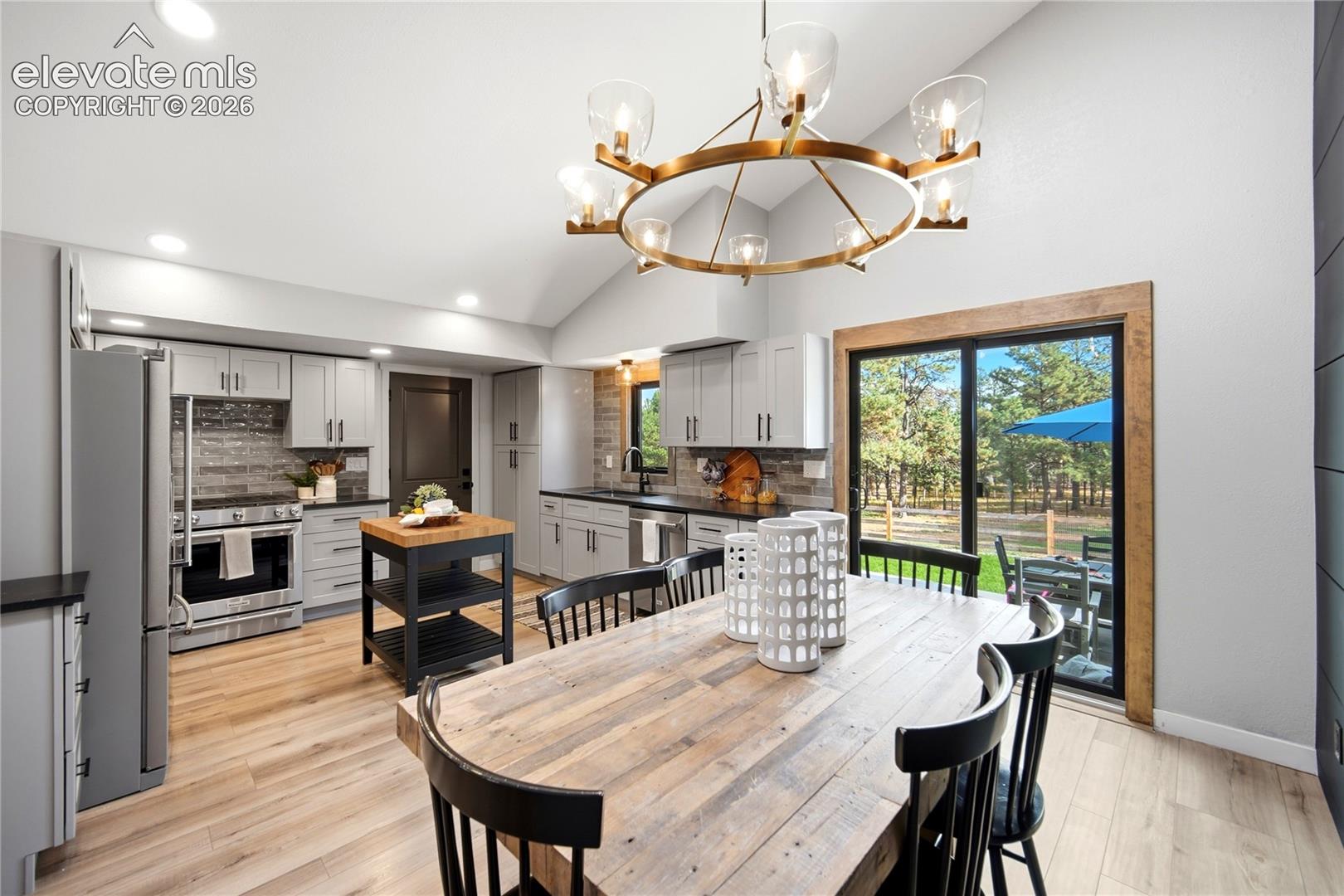 Kitchen featuring light gray cabinetry, stainless steel appliances, wood-finish flooring, vaulted ceilings, and a circular wagon wheel chandelier