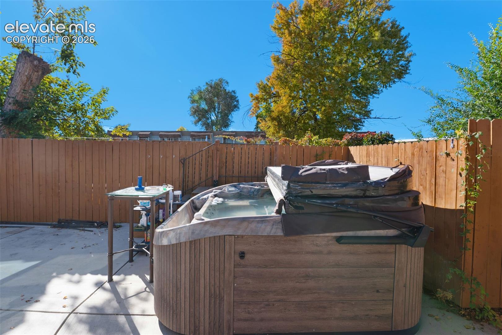 Private outdoor area featuring a concrete patio, a plumbed hot tub with wood-finish siding, and full-height wood fencing