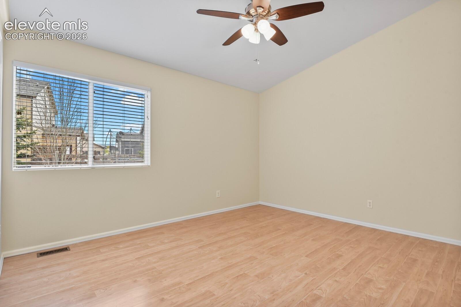 Spacious room featuring vaulted ceilings, a ceiling fan with integrated lighting, a large window with blinds, and wood-finish flooring