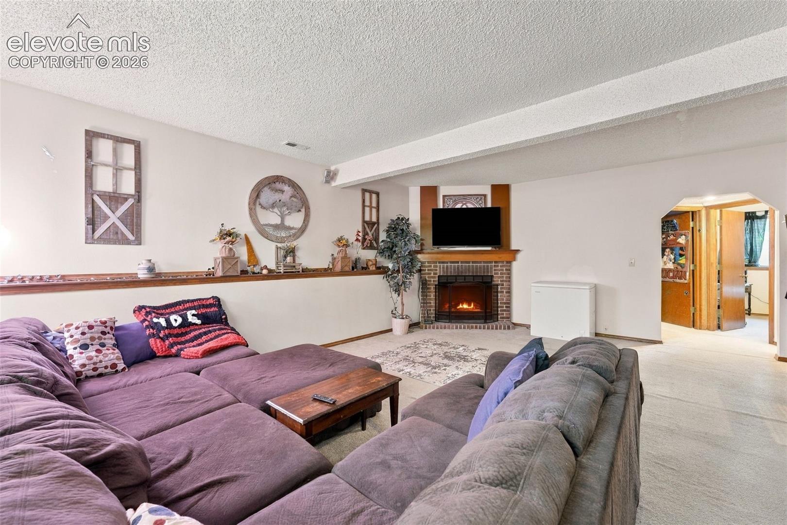 Corner fireplace with a brick surround, wood mantel, arched entryway, and integrated chair rail shelving