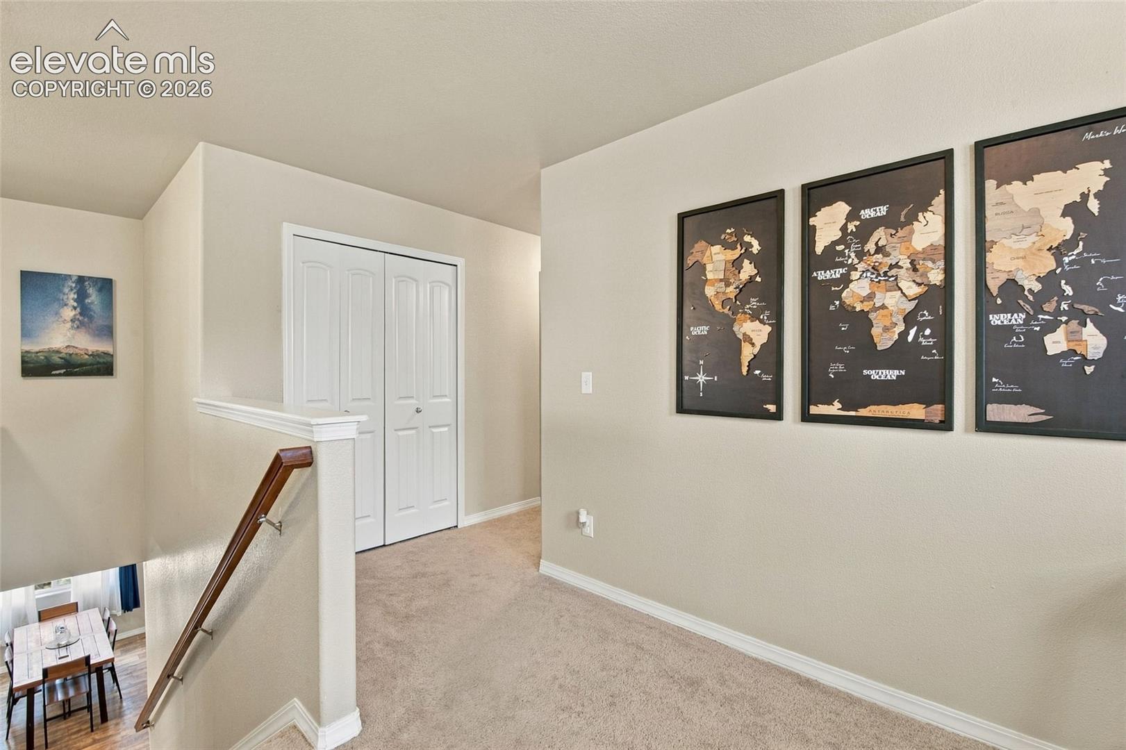 Hallway featuring carpeting, wood-finish handrail with metallic balusters, and bi-fold doors