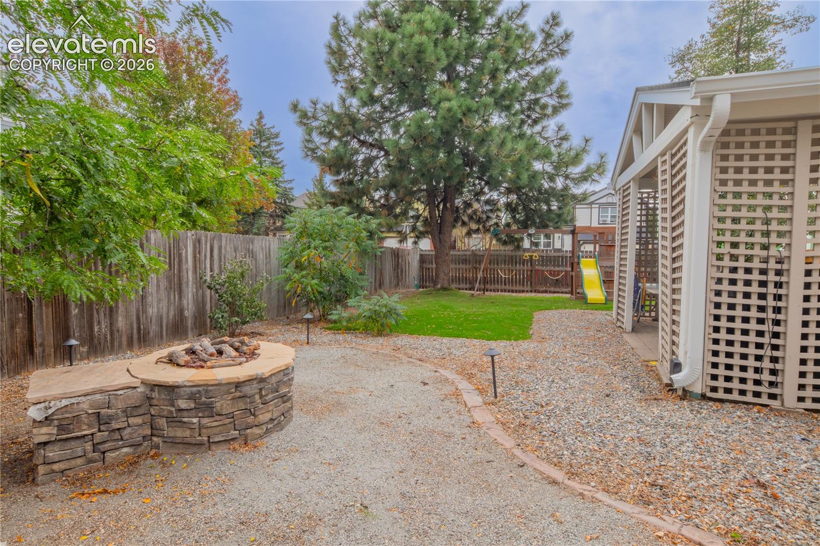 Backyard featuring a stone-clad fire pit with an integrated stone bench, gravel ground cover, and a manicured lawn area