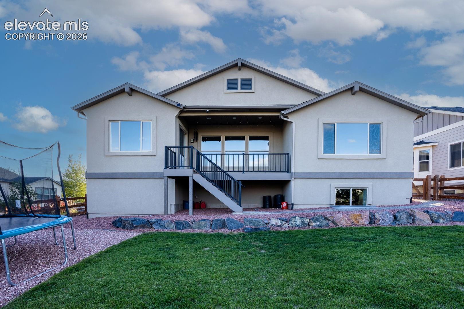 Exterior rear elevation featuring stucco siding, a raised deck with metal railings, a staircase leading to the rear yard, and decorative rock landscape borders