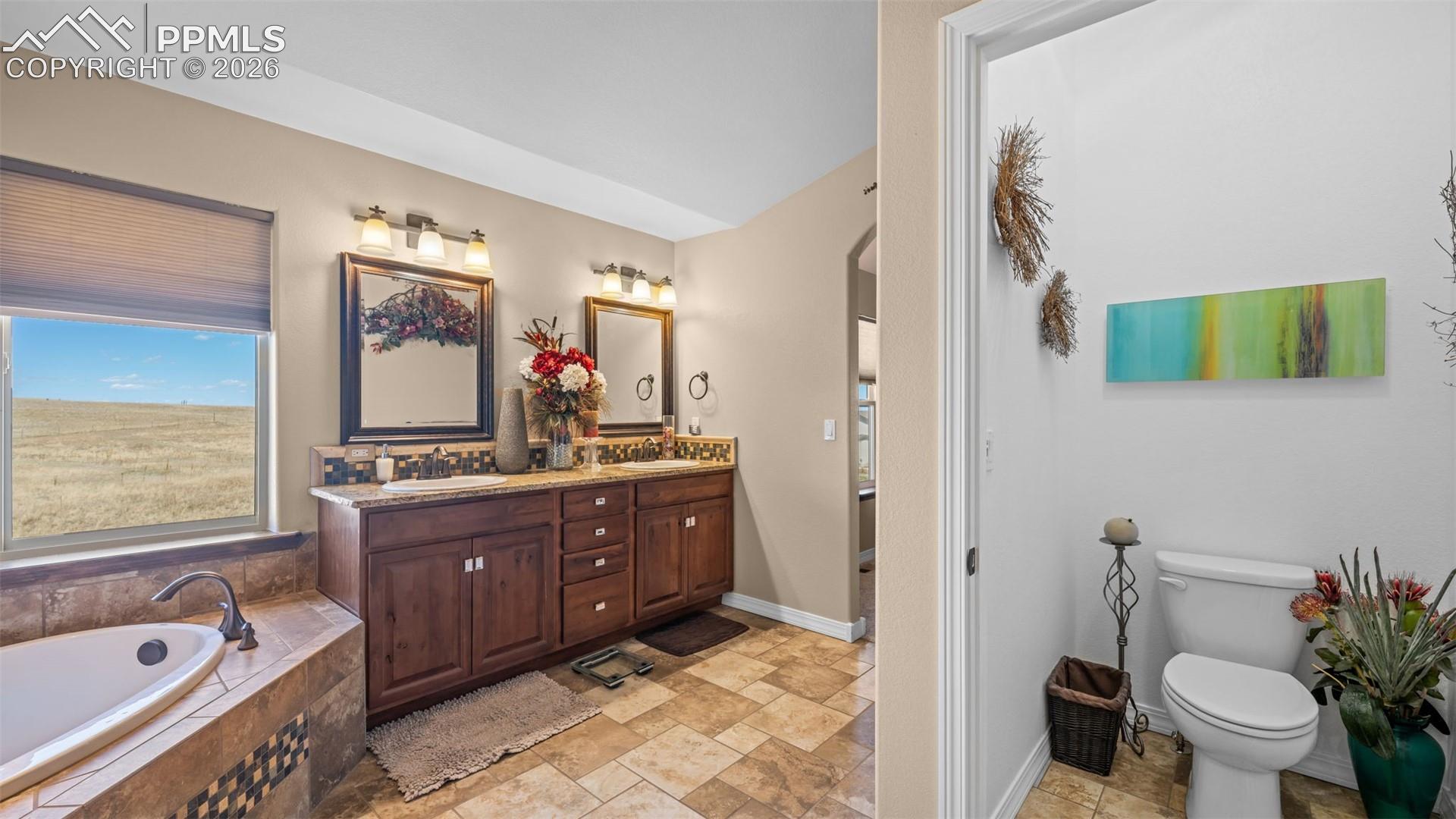 Bathroom with double vanity, a garden tub, and light stone finish flooring