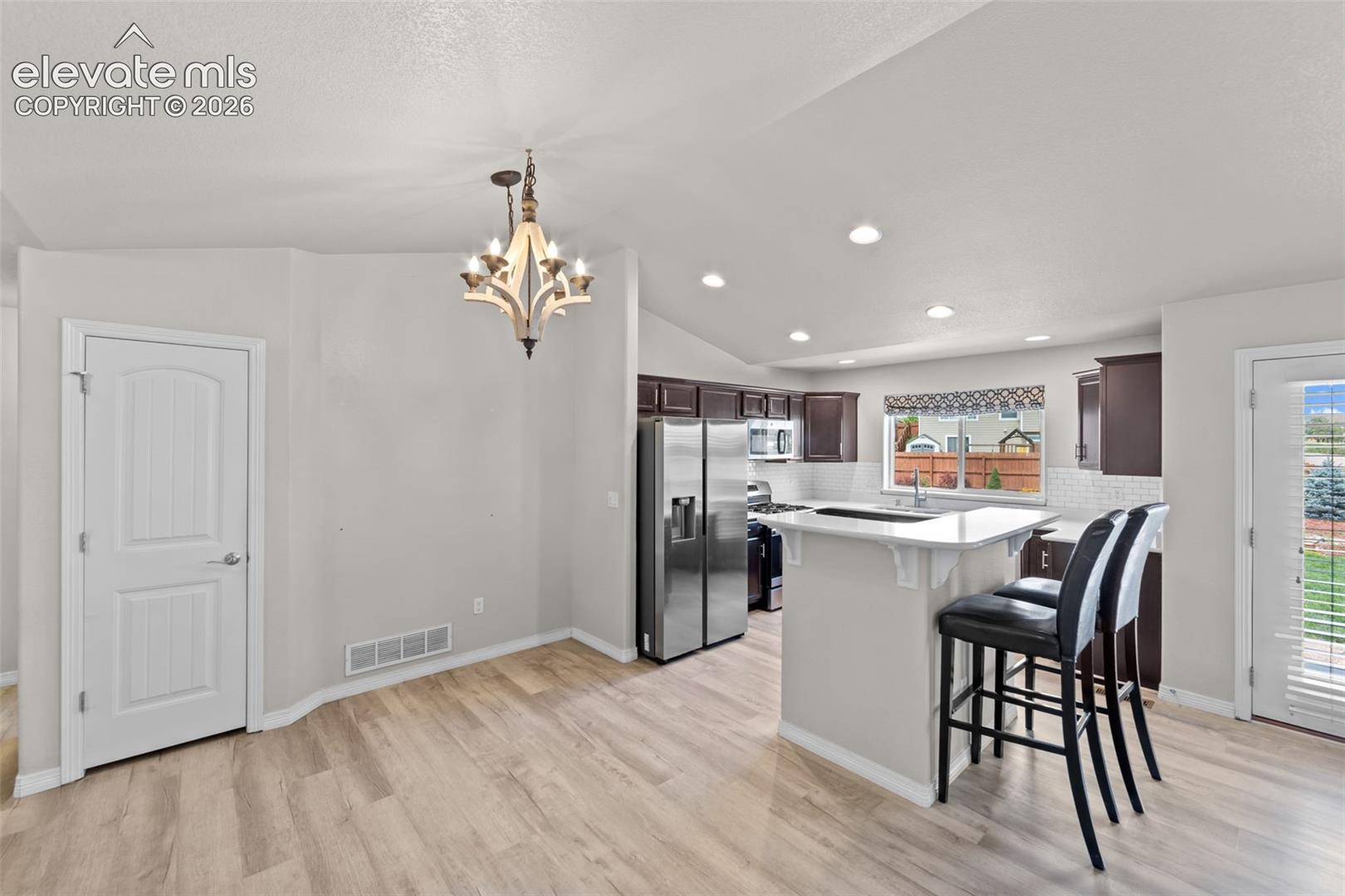 Open-concept kitchen and dining area featuring stainless steel appliances, a large center island with seating for two, wood-finish flooring throughout, recessed lighting, and a decorative pendant fixture