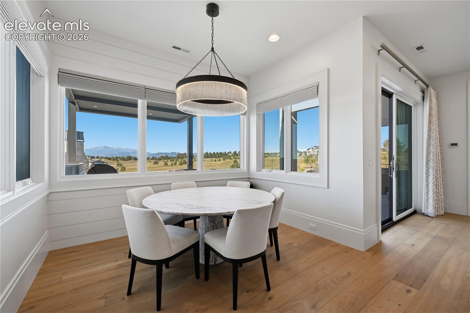 Horizontal shiplap wall paneling, wood-finish flooring, large picture windows, mountain and landscape scenery, and a circular drum pendant light fixture