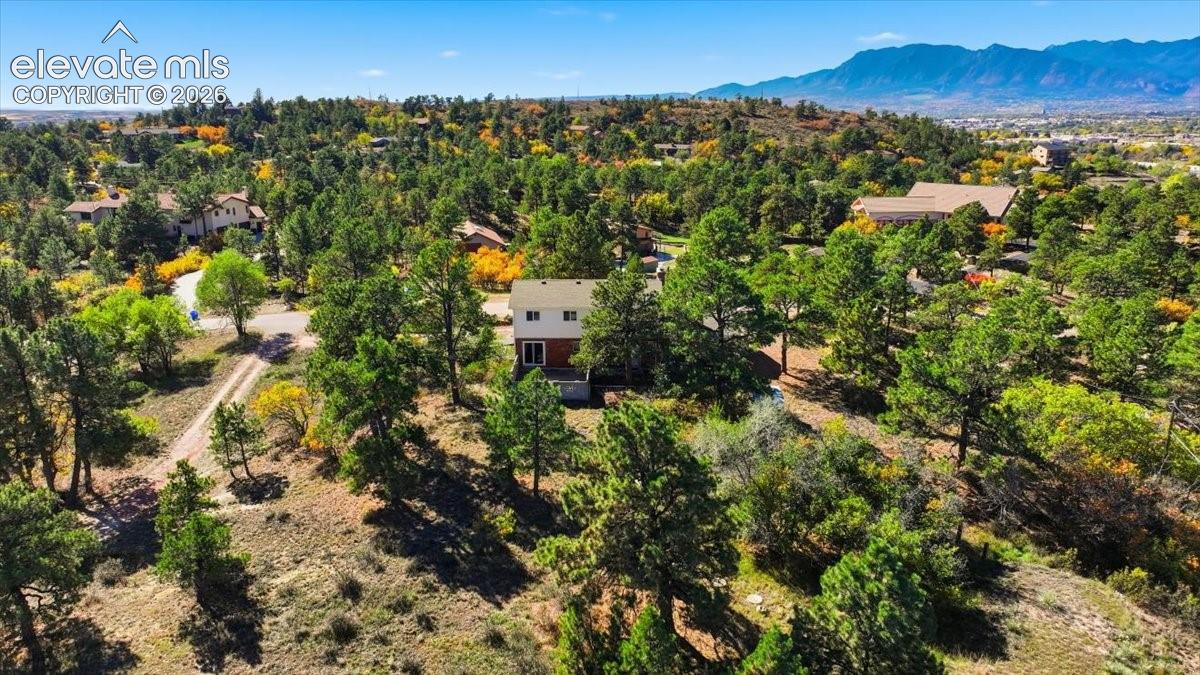 Multi-level residence situated on a wooded lot featuring mature coniferous trees and prominent mountain backdrops