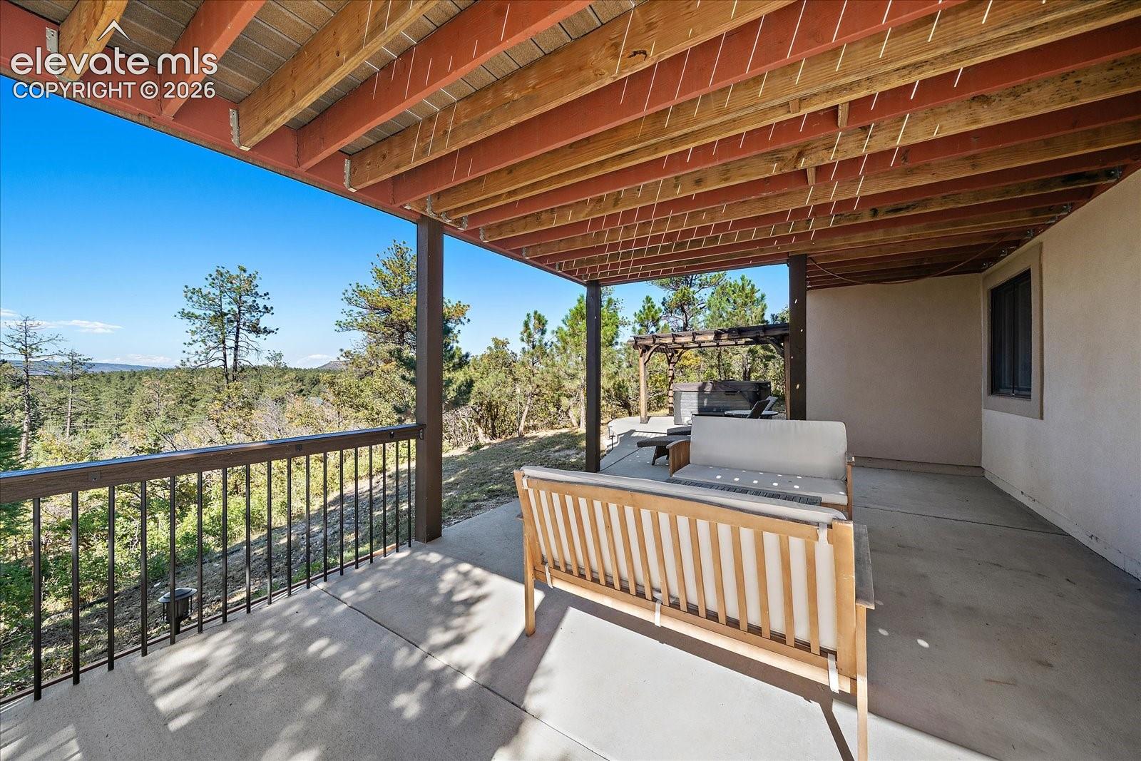 Covered concrete patio featuring exposed wood-beam ceiling, metal railing, and natural woodland surroundings
