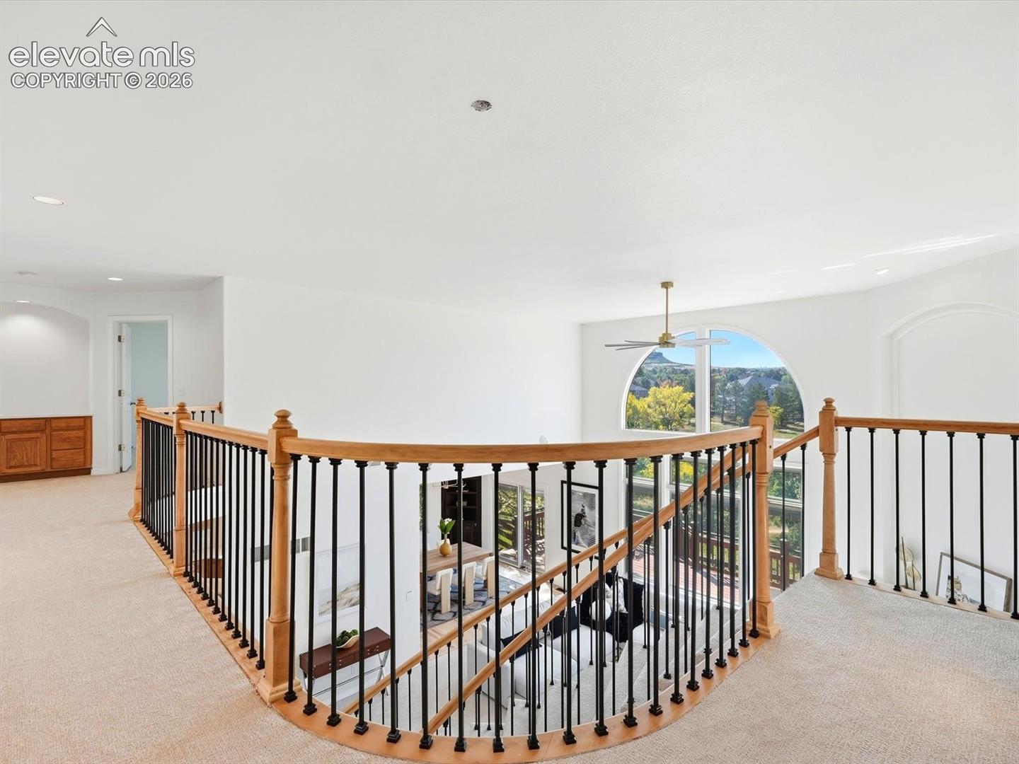 Curved landing featuring a light wood railing with black metal balusters and a large arched window