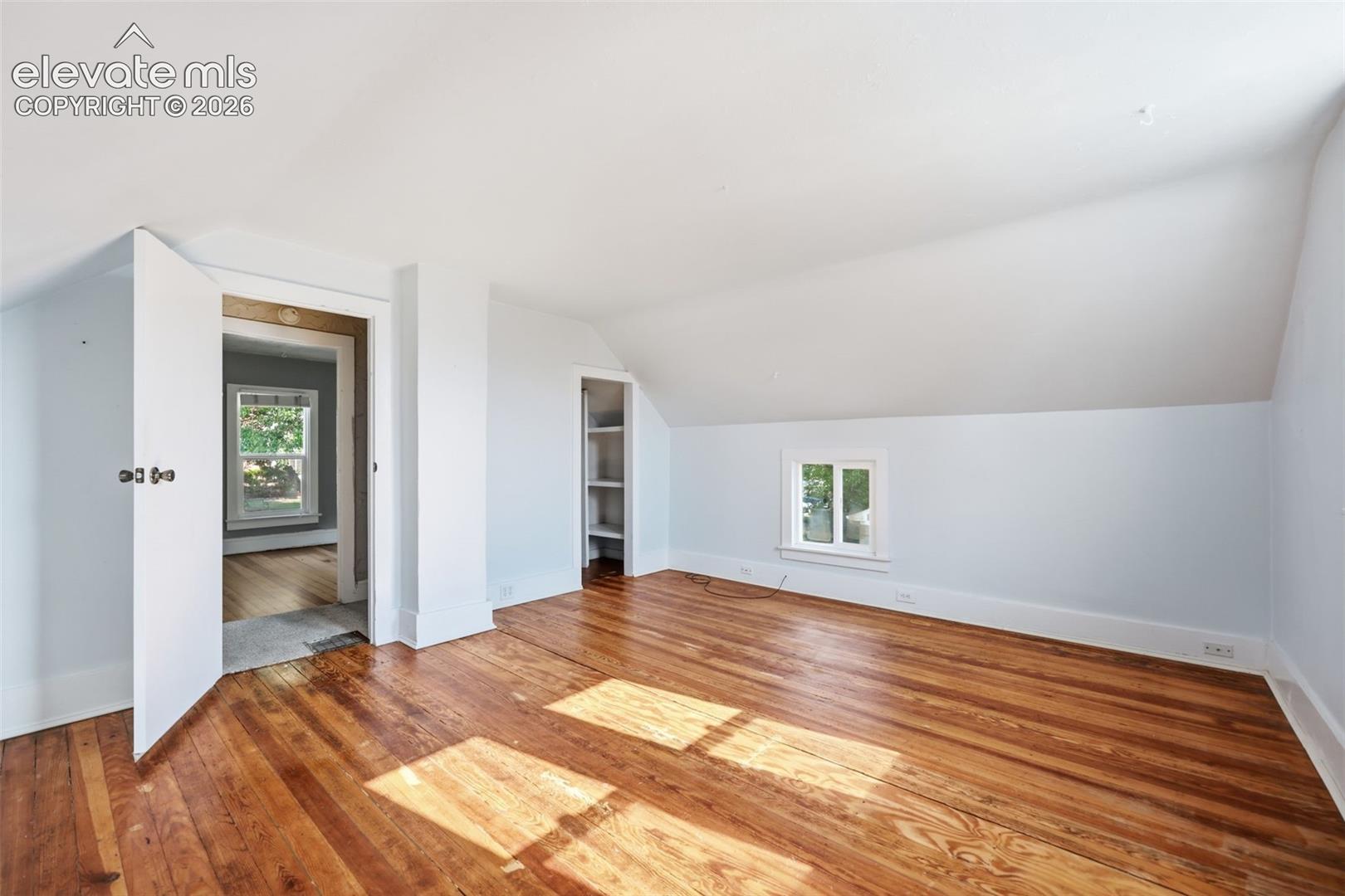 Primary bedroom with pine hardwood flooring, painted walls, sloped ceilings, walk-in closet with built-in shelving, and a window.