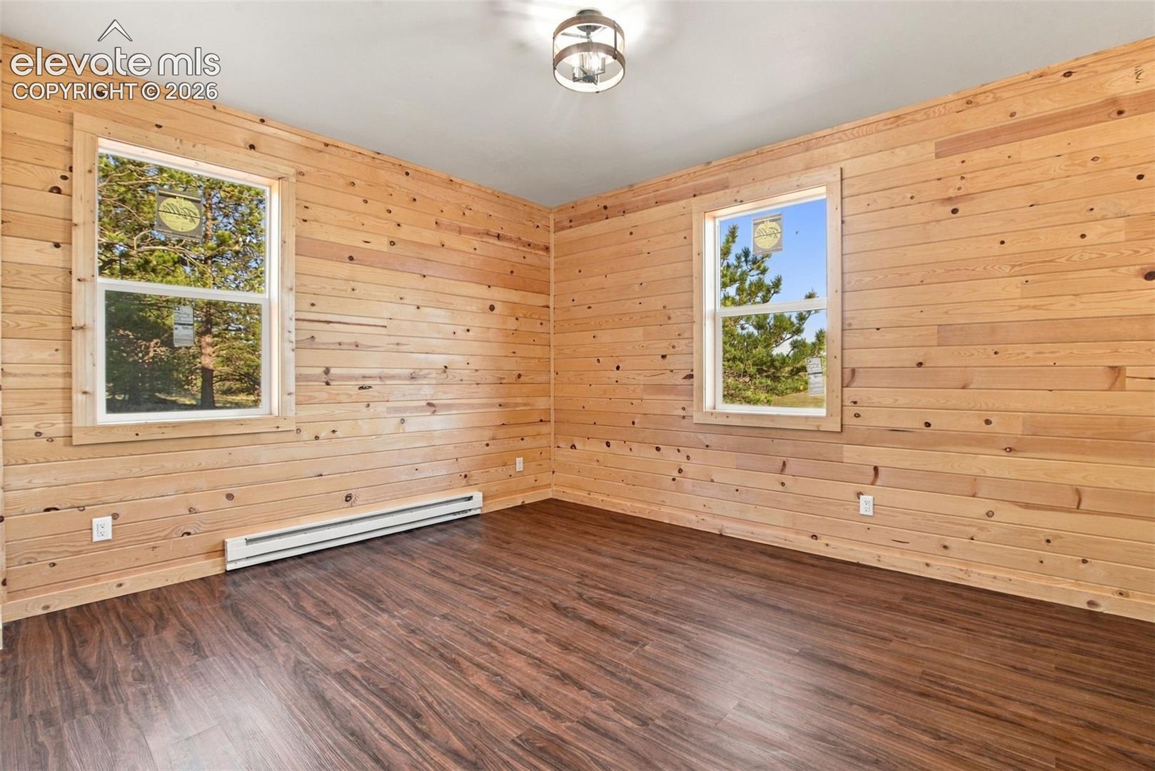 Interior space featuring knotty wood wall paneling, wood-finish flooring, two large windows, and a flush-mount industrial-style ceiling fixture