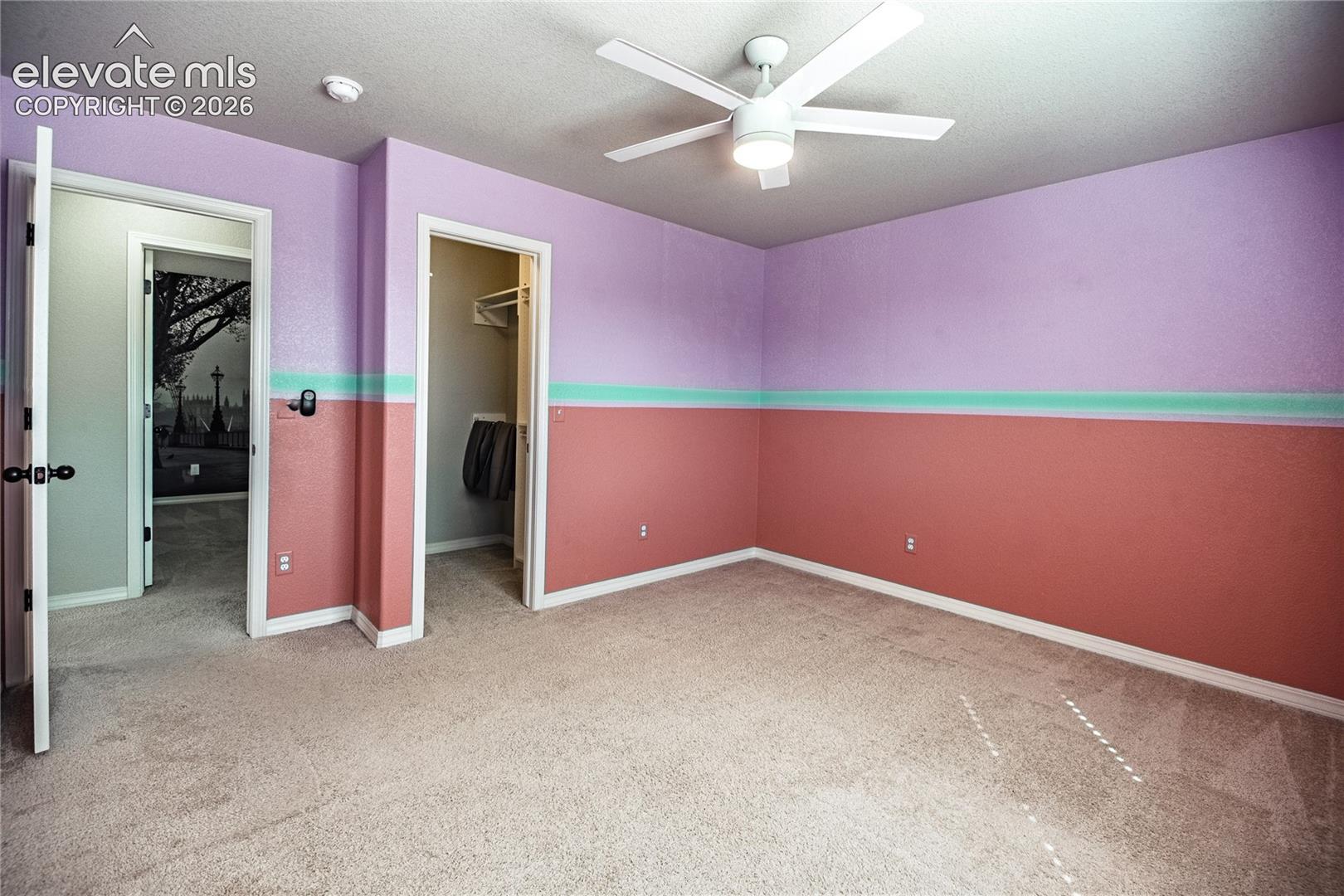 Textured wall finishes with a decorative accent stripe, ceiling fan, and plush carpet flooring