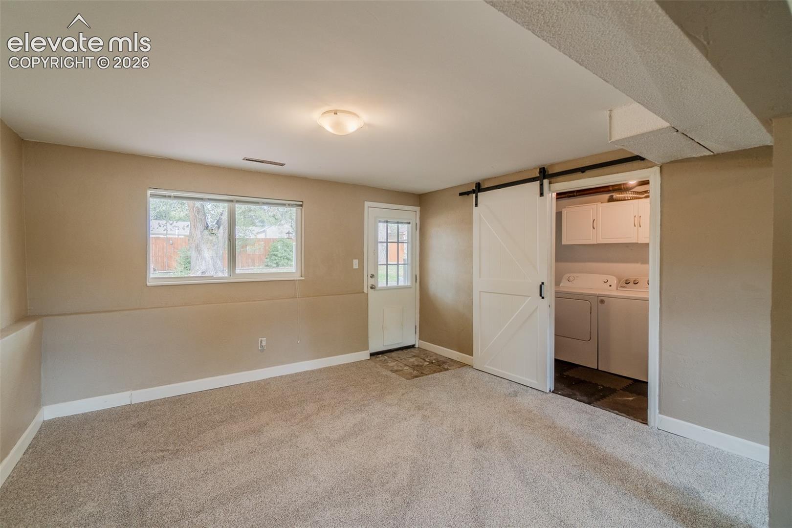 Carpeted room with a barn door entry to a utility area featuring white cabinetry and appliances