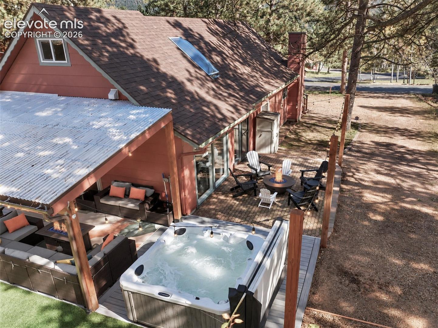 Exterior featuring a covered patio with corrugated metal roofing, a built-in hot tub on a composite deck, a brick-paved patio area, and an integrated skylight