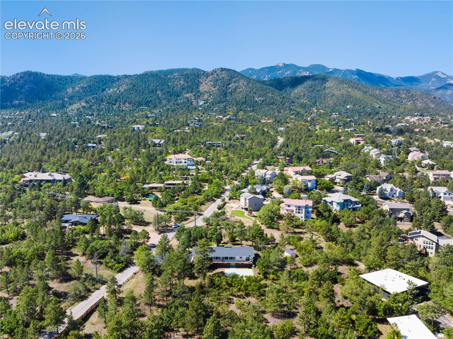 Aerial perspective featuring a hillside location surrounded by dense evergreen forest and expansive mountain terrain