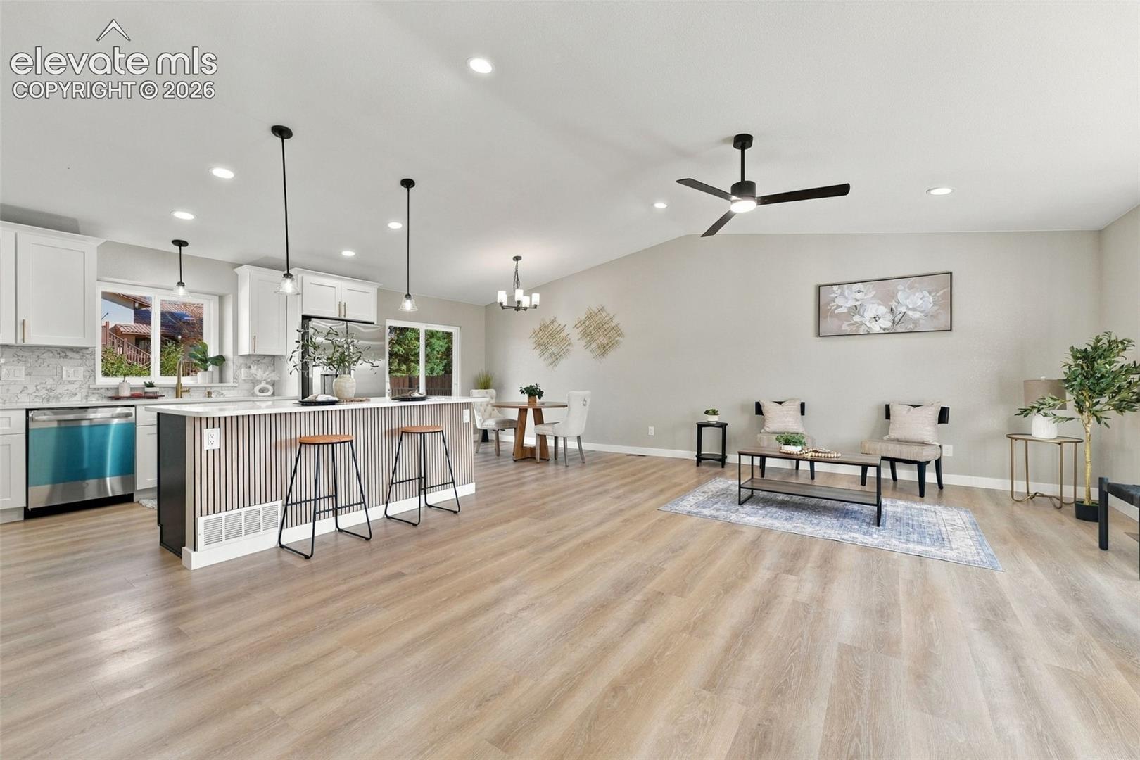 Open-concept interior featuring light wood-finish flooring, white cabinetry, a kitchen island with vertical slat detailing, recessed lighting, and a ceiling fan