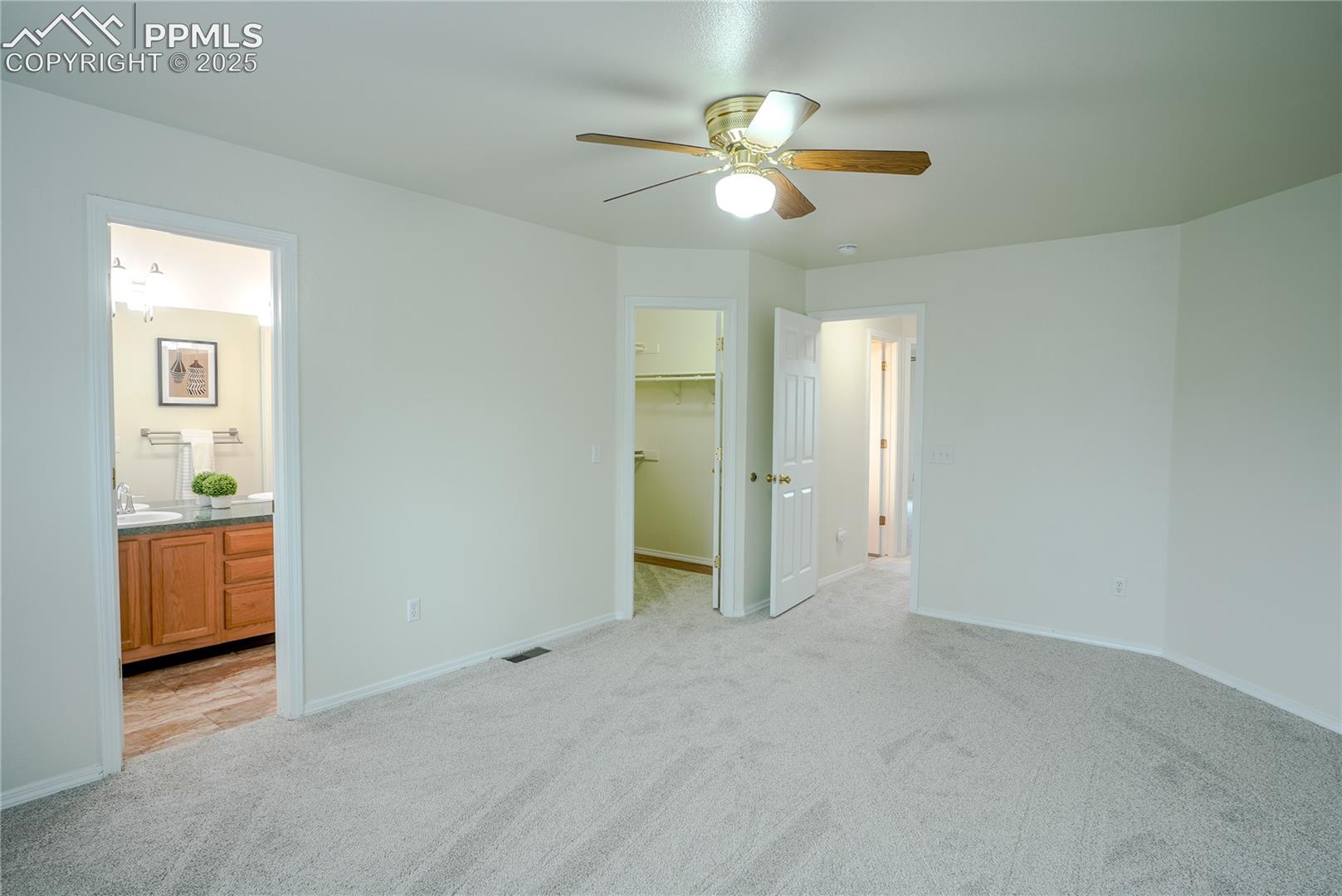 Primary bedroom featuring a spacious closet, light carpet, ceiling fan, and ensuite bathroom