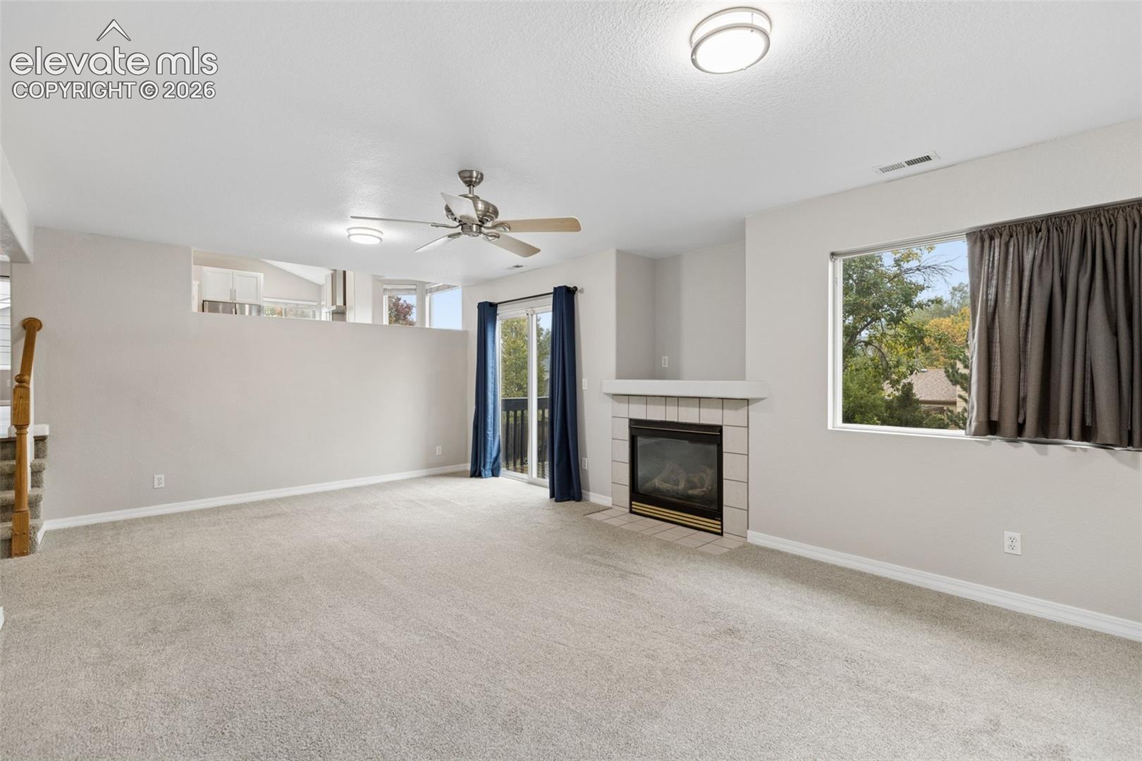 Neutral-toned living space featuring a fireplace with tile surround, sliding glass door, ceiling fan, and carpeted flooring