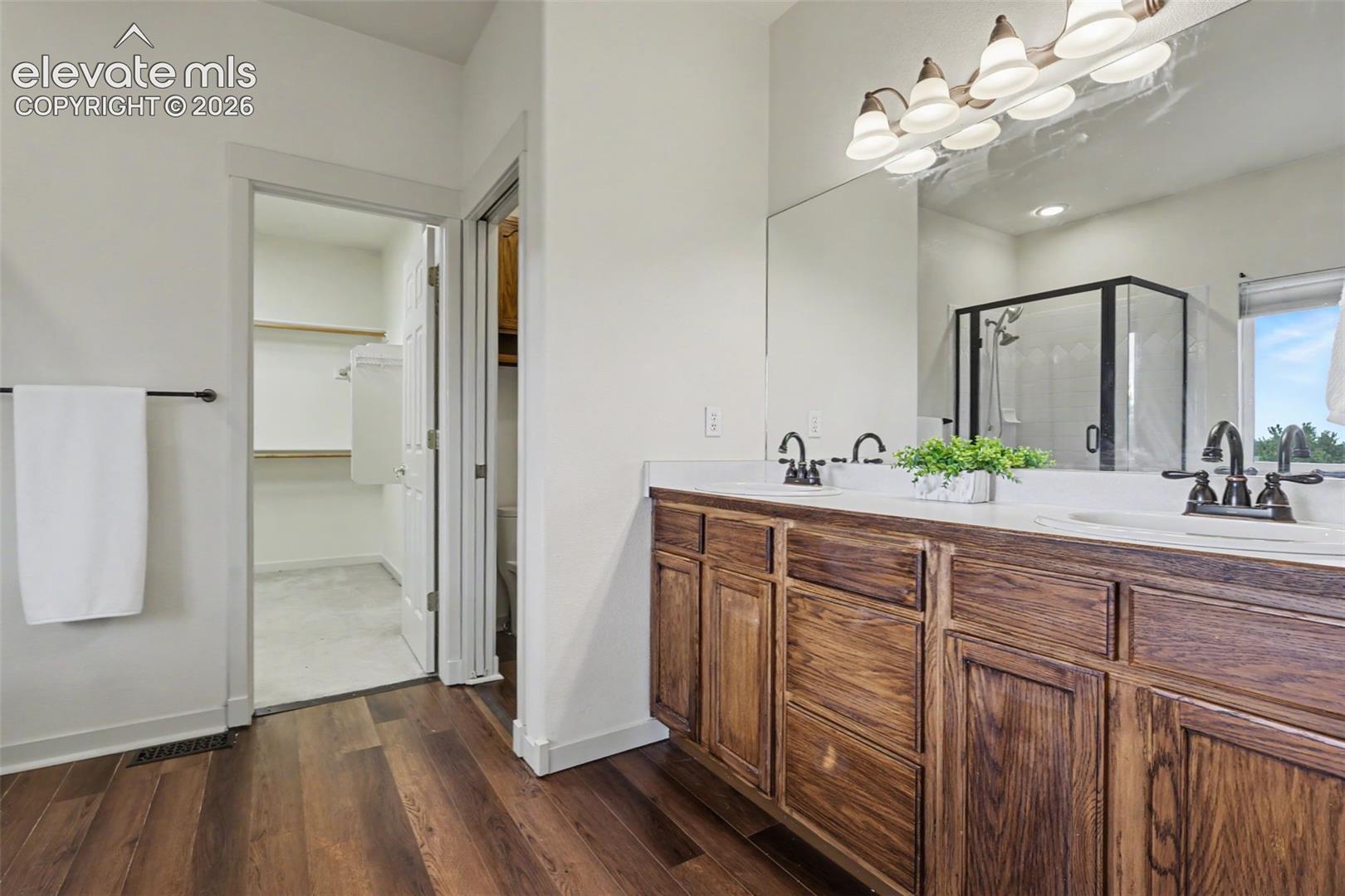 Bathroom featuring a dual vanity with wood-finish cabinetry, white countertops, and matte black fixtures