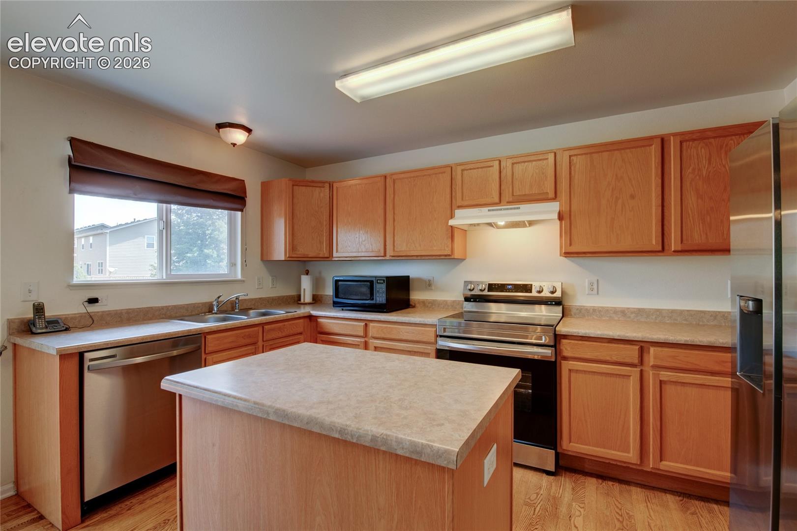 Kitchen featuring a center island, light wood cabinetry, light-toned countertops, a stainless steel dishwasher, and a stainless steel range with overhead ventilation