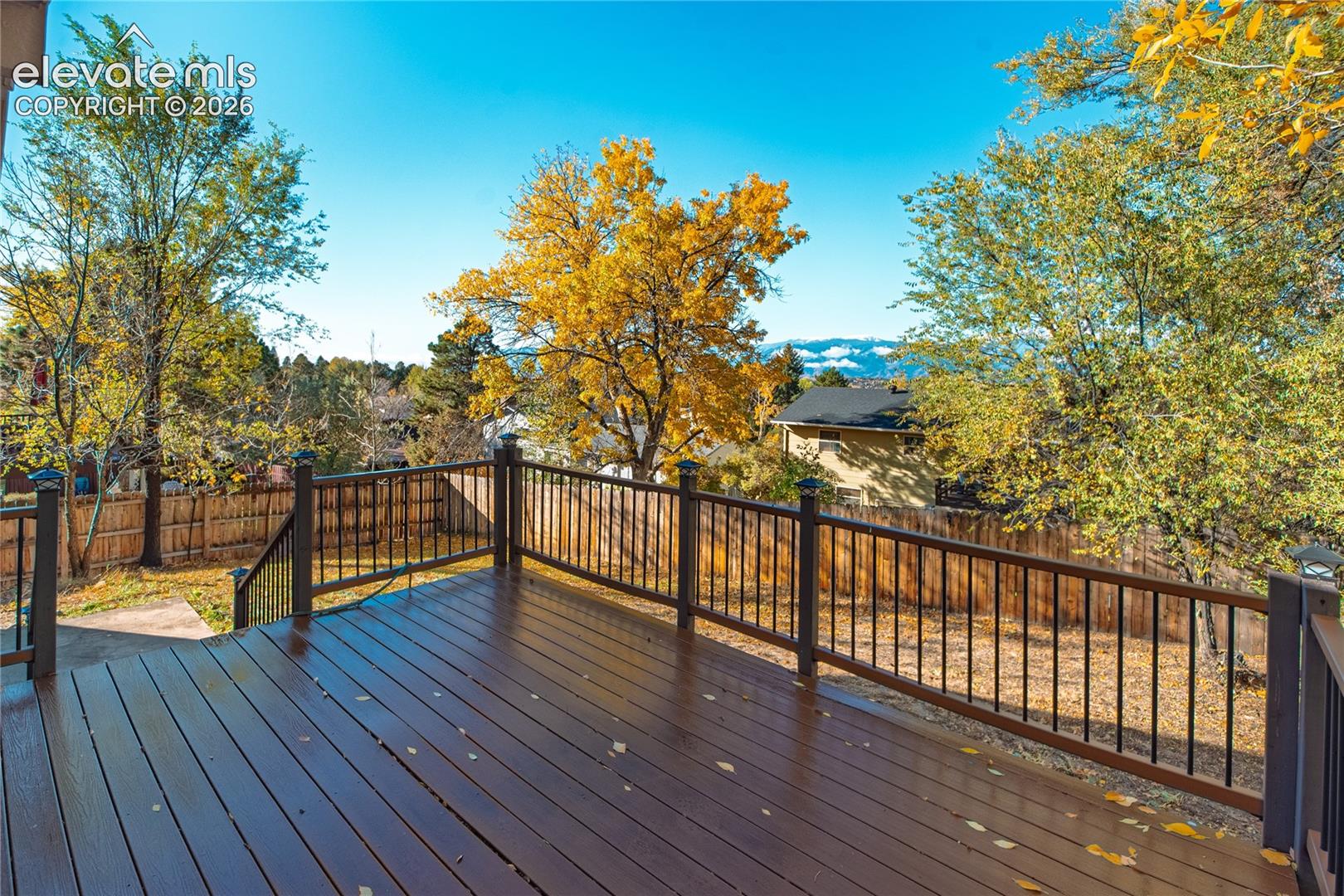 Elevated wood-finished deck with metal railing, privacy fencing, and mountain backdrop