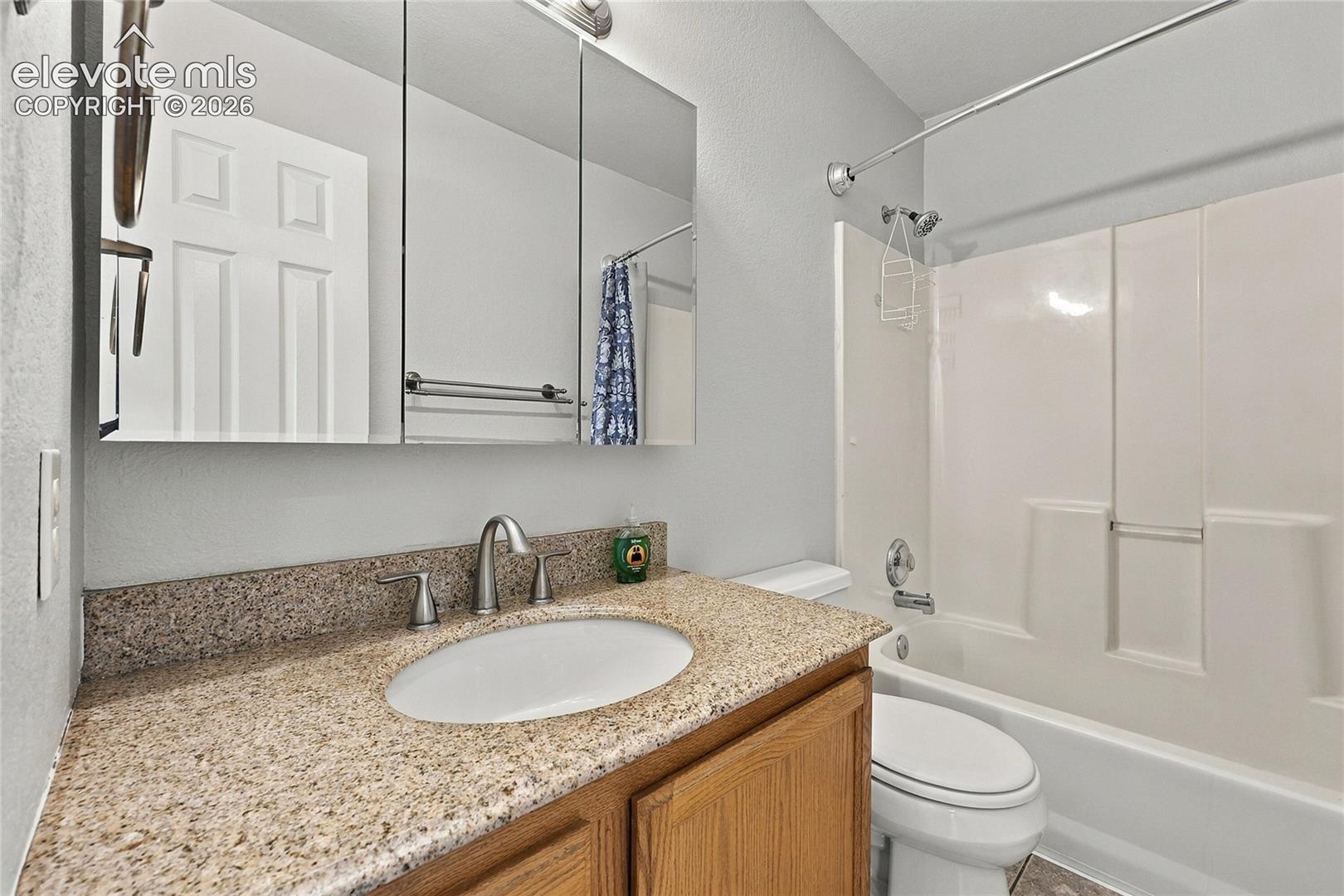 Bathroom featuring a wood-finish vanity with a stone-composite countertop, integrated oval sink, mirrored medicine cabinet, and a combination tub and shower enclosure with a metallic shower rod