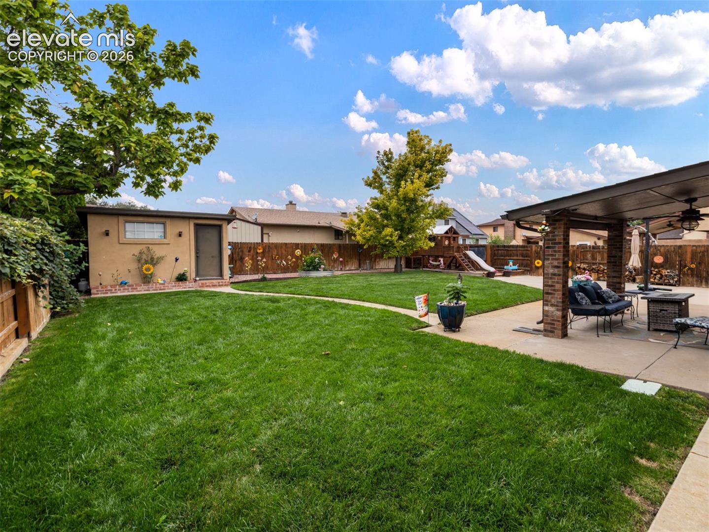 Expansive backyard with a green lawn, covered patio, stucco shed, and wood fencing