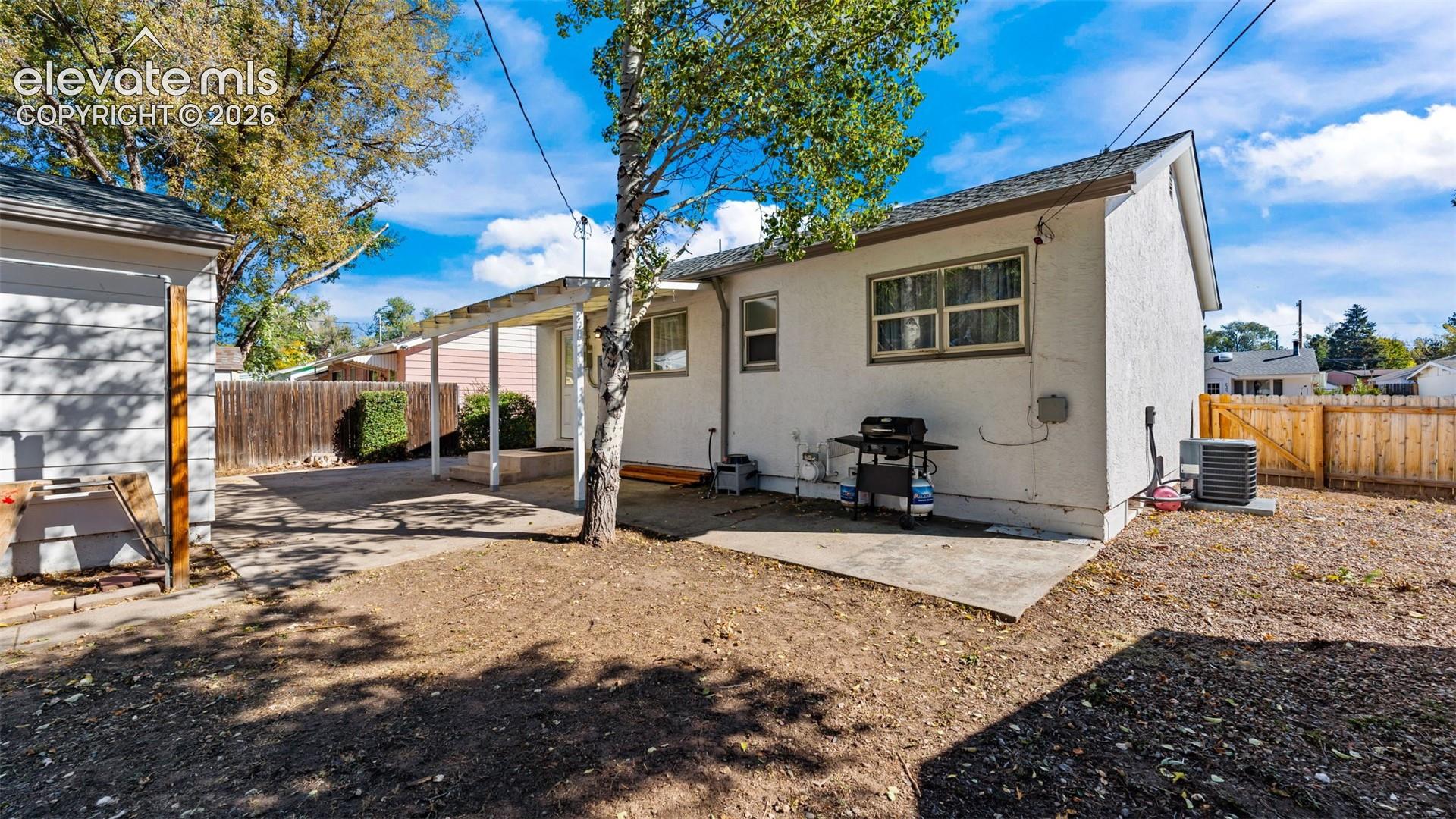 Exterior features include a stucco finish, a covered patio with support columns, and perimeter wood fencing