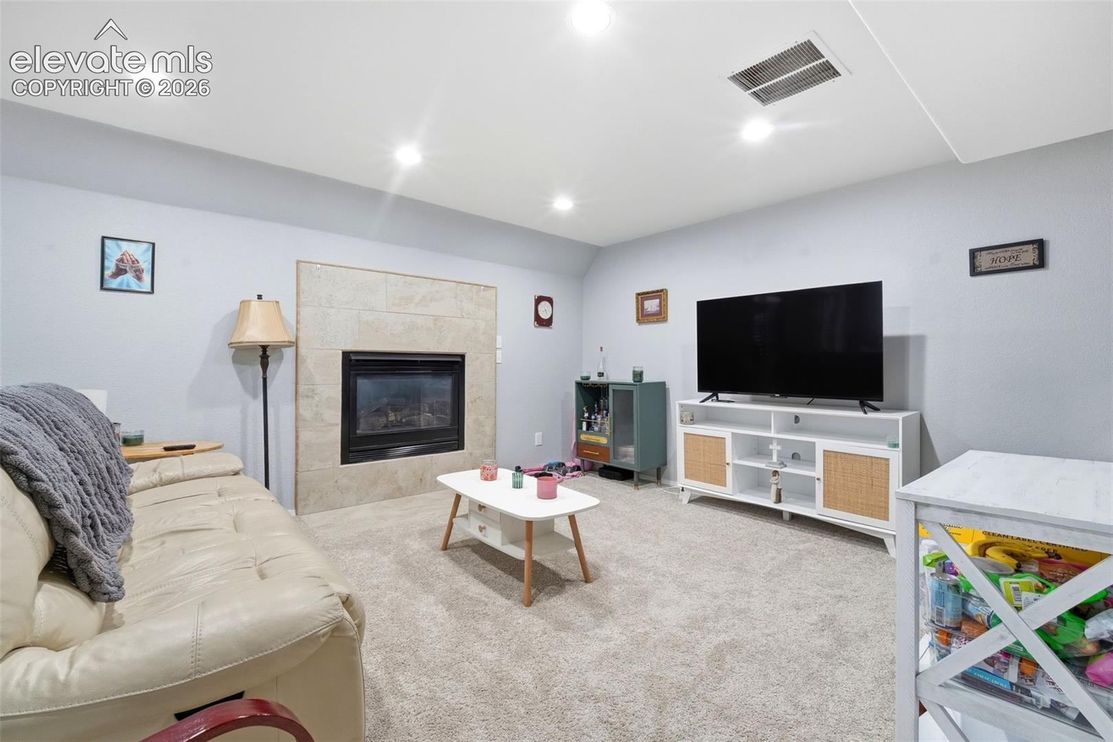 Recessed lighting illuminates a carpeted living space featuring a tile-surround fireplace